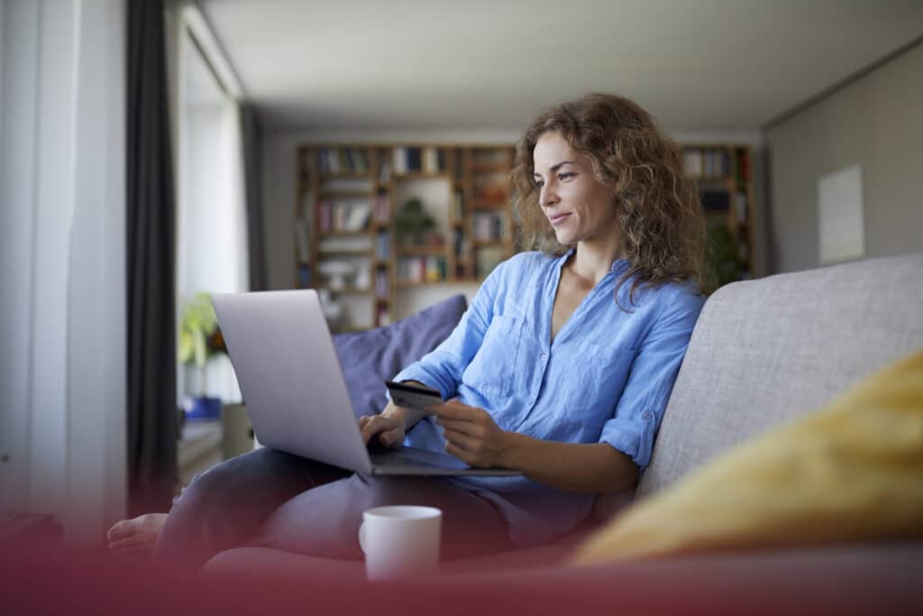 Smiling woman doing online shopping on laptop at home Fiatal nő kanapén ülve laptopot használ, banki szolgáltatást vesz igénybe